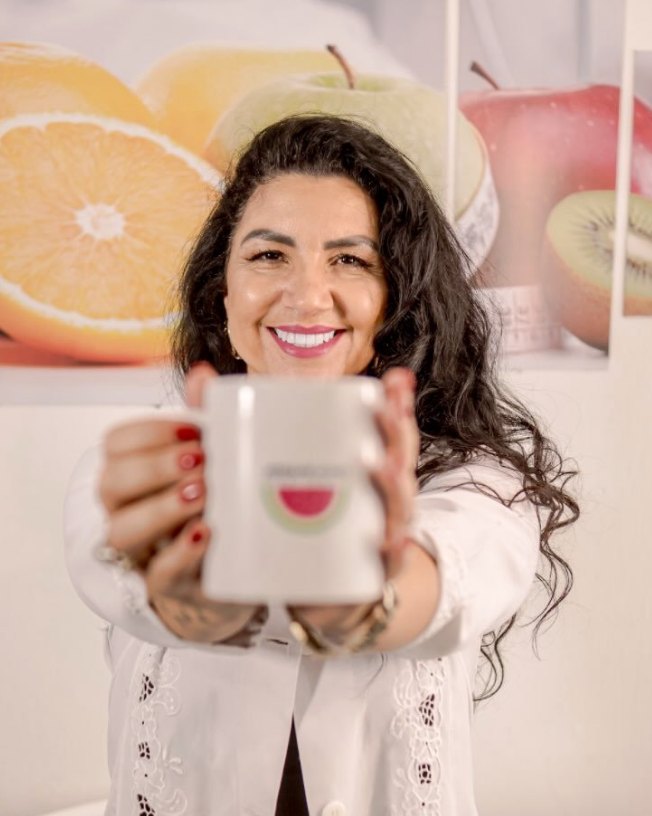 Josiane Nunes, nutricionista, sorrindo e segurando uma caneca com o logo dela